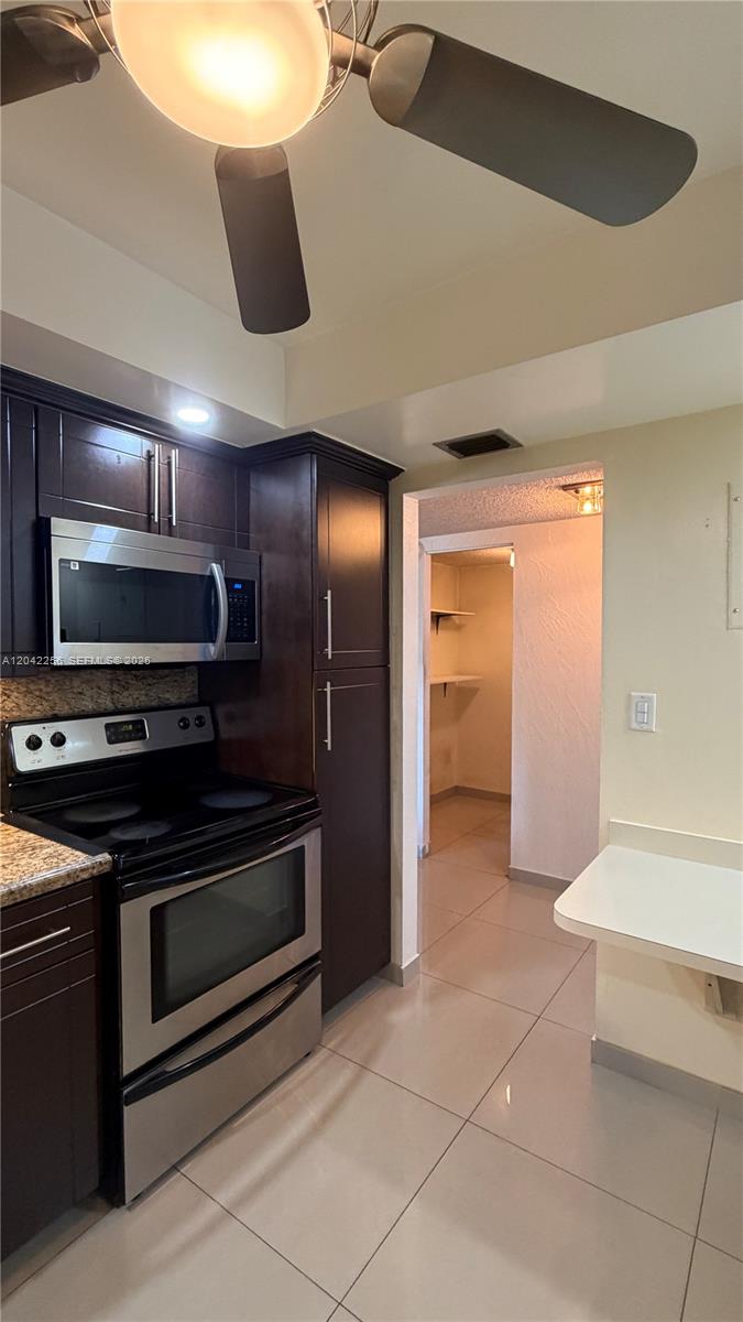 A kitchen features dark wood cabinets, stainless steel appliances, and light-colored tile flooring — 3280 Spanish Moss Ter # 214, Lauderhill FL 33319, LAUDERHILL, FL