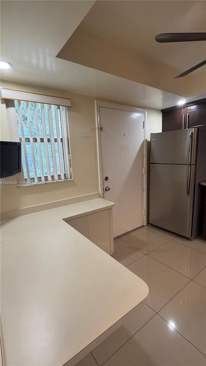 A kitchen features a white countertop, a refrigerator, a window with blinds, and tile flooring — 3280 Spanish Moss Ter # 214, Lauderhill FL 33319, LAUDERHILL, FL