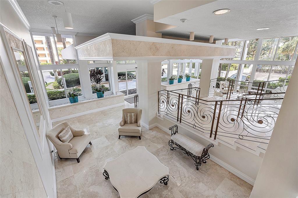 A high-angle view of a lobby featuring stone floors, ornate metal railings, and seating areas — 1620 S Ocean Boulevard # 7K, Pompano Beach FL 33062, POMPANO BEACH, FL
