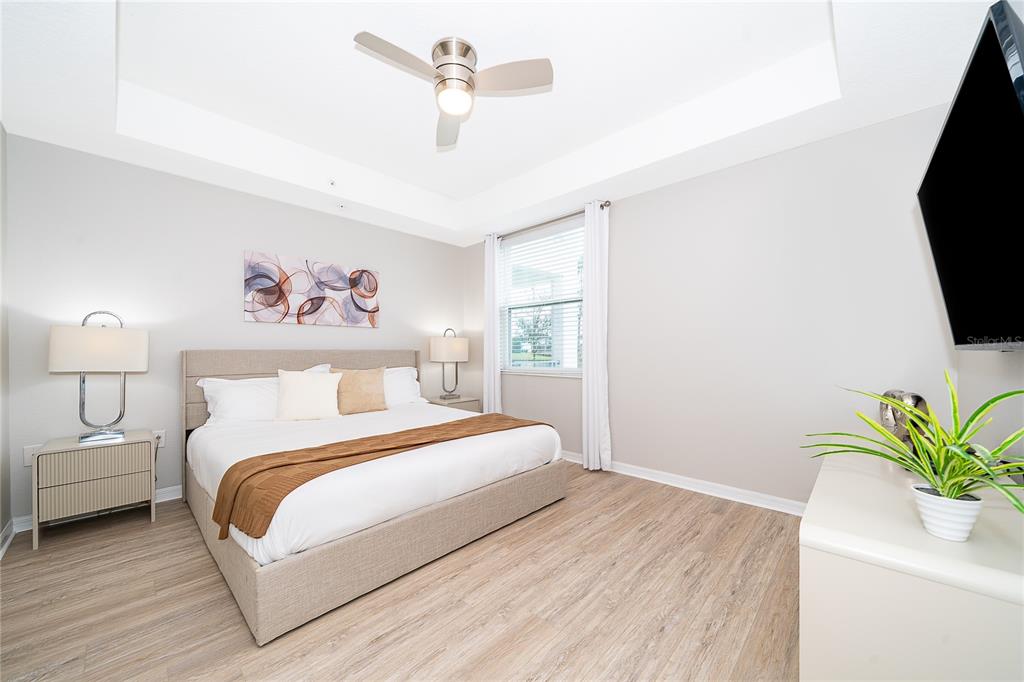A bedroom features a king bed, light wood flooring, a ceiling fan, and a television — 3131 PARADOX CIRCLE UNIT 108, KISSIMMEE, FL