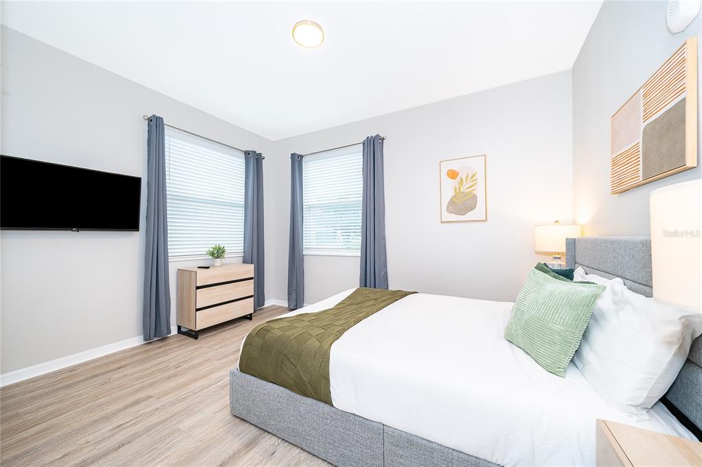 A bedroom features a gray upholstered bed, light wood flooring, and two windows with curtains — 3131 PARADOX CIRCLE UNIT 108, KISSIMMEE, FL