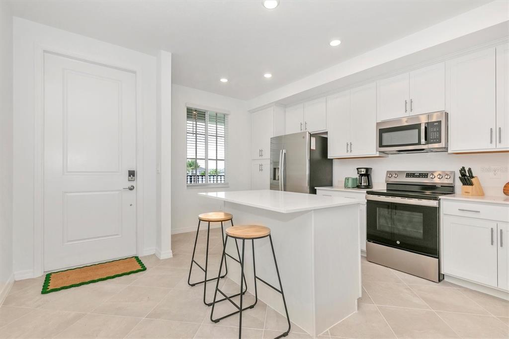 A modern kitchen features white cabinets, stainless steel appliances, a center island, and tile flooring — 12320 WELLEN GOLF STREET UNIT 204, VENICE, FL