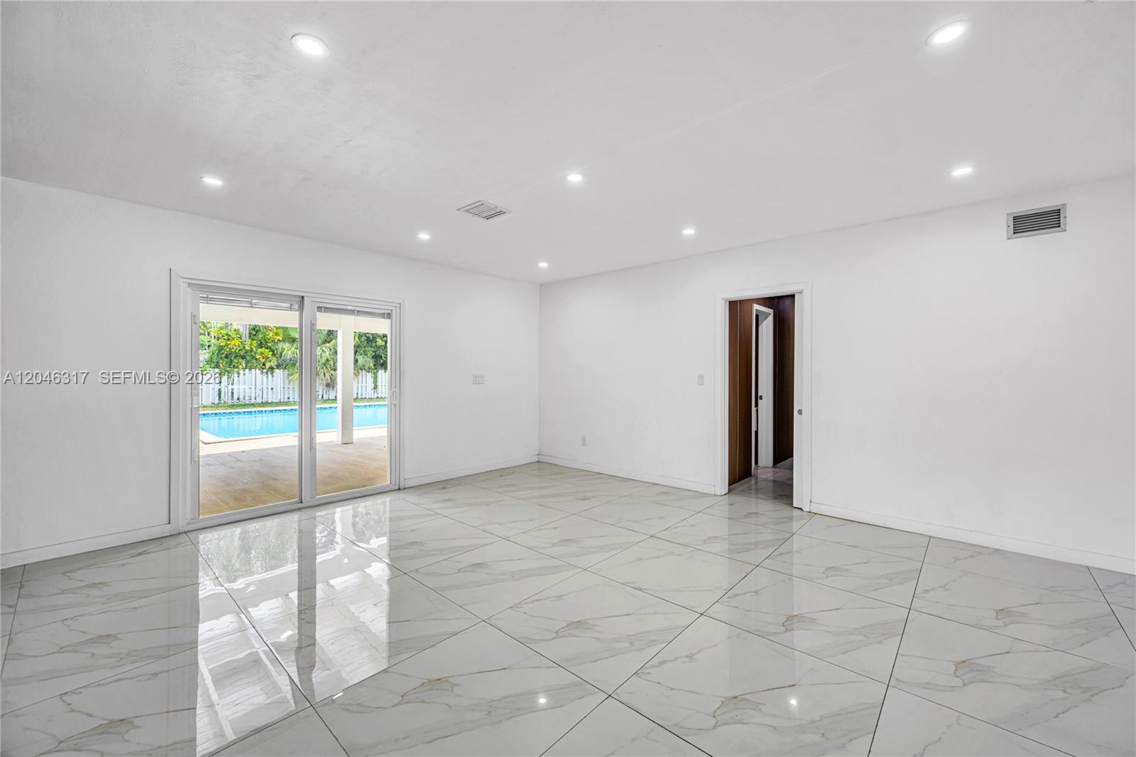 A bright room features white walls, large marble-look floor tiles, and sliding glass doors — 12525 SW 68th Ct, Pinecrest FL 33156, PINECREST, FL