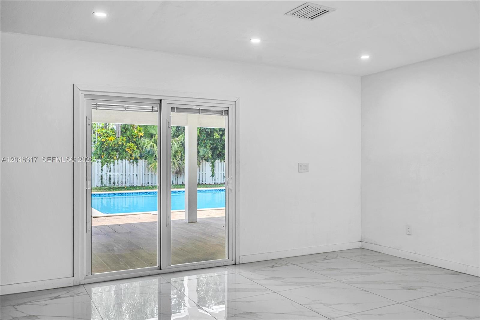 A bright room with white walls, marble-style tile flooring, and sliding doors overlooking a pool — 12525 SW 68th Ct, Pinecrest FL 33156, PINECREST, FL