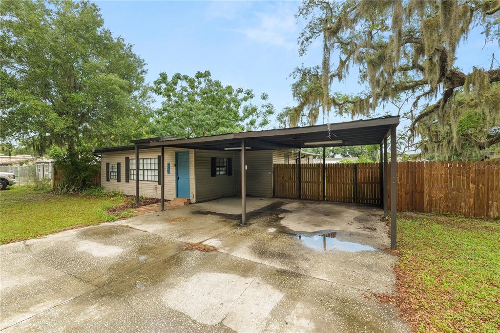 A single-story house with a blue front door, a large carport, and a wooden fence — 124 GRIFFIN AVENUE, LAKELAND, FL