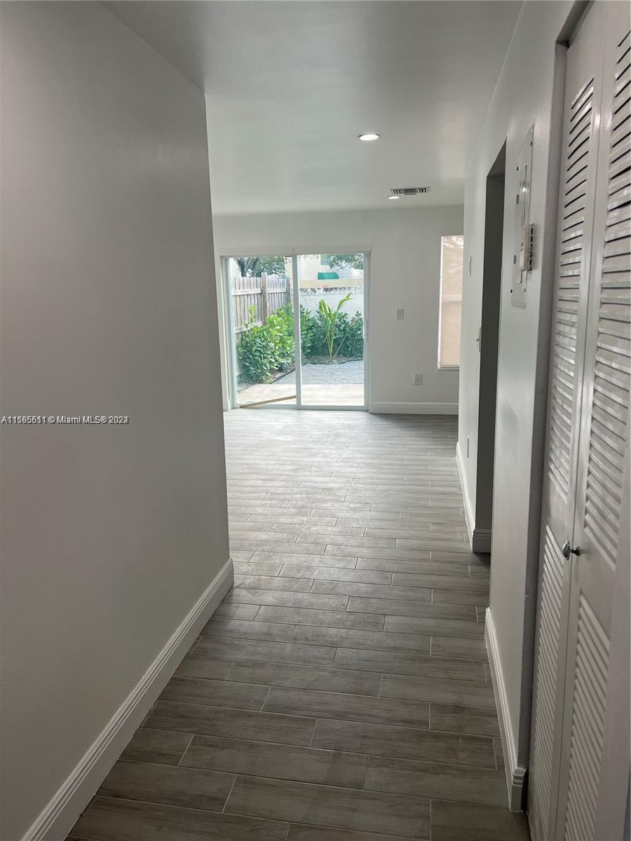 A hallway with light wood-look tile flooring leads to a living area with sliding glass doors — 2050 SW 122nd Ave # 22, Miami FL 33175, MIAMI, FL