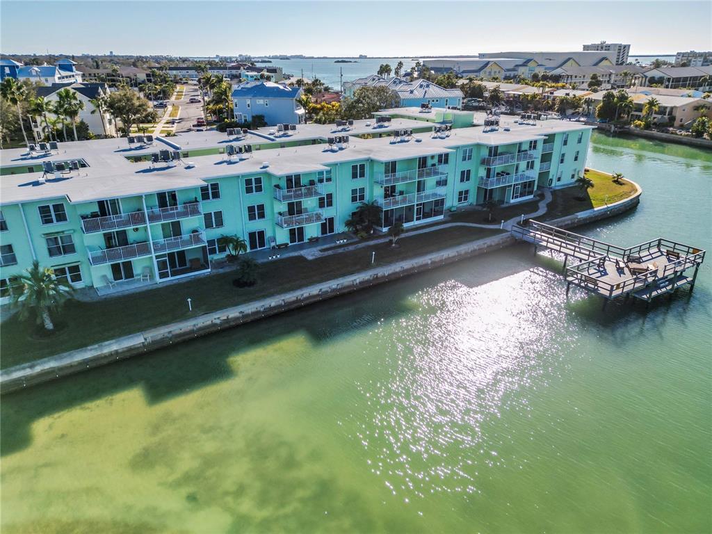 An aerial view shows a light green multi-story apartment building situated along a waterfront — 464 N PAULA DRIVE UNIT 115, DUNEDIN, FL