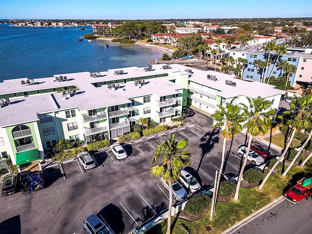 An aerial view shows a multi-story apartment building with a parking lot and waterfront access — 464 N PAULA DRIVE UNIT 115, DUNEDIN, FL