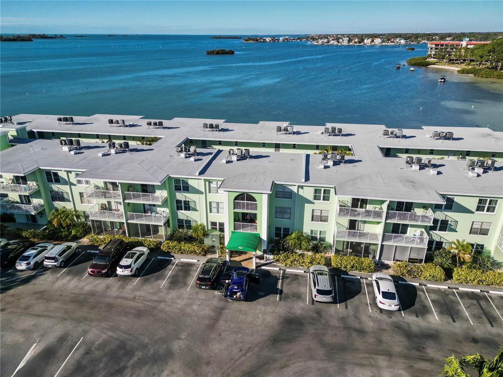 An aerial view shows a multi-story apartment building with a parking lot and waterfront access — 464 N PAULA DRIVE UNIT 115, DUNEDIN, FL