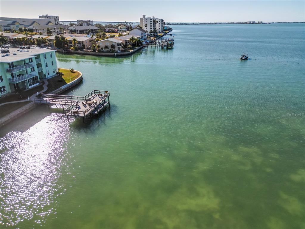 An aerial view shows a wooden pier extending into a bay near waterfront residential buildings — 464 N PAULA DRIVE UNIT 115, DUNEDIN, FL