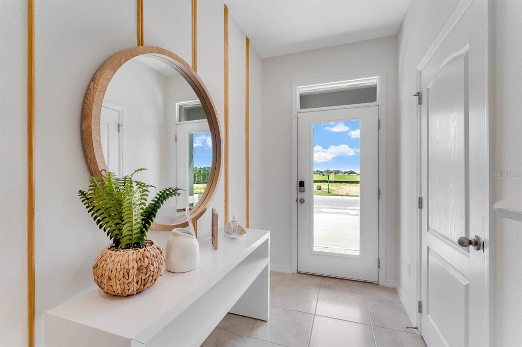 A bright entryway features a white console table, a round mirror, and a glass-paneled door — 2634 OLYMPIC COURT, DAVENPORT, FL