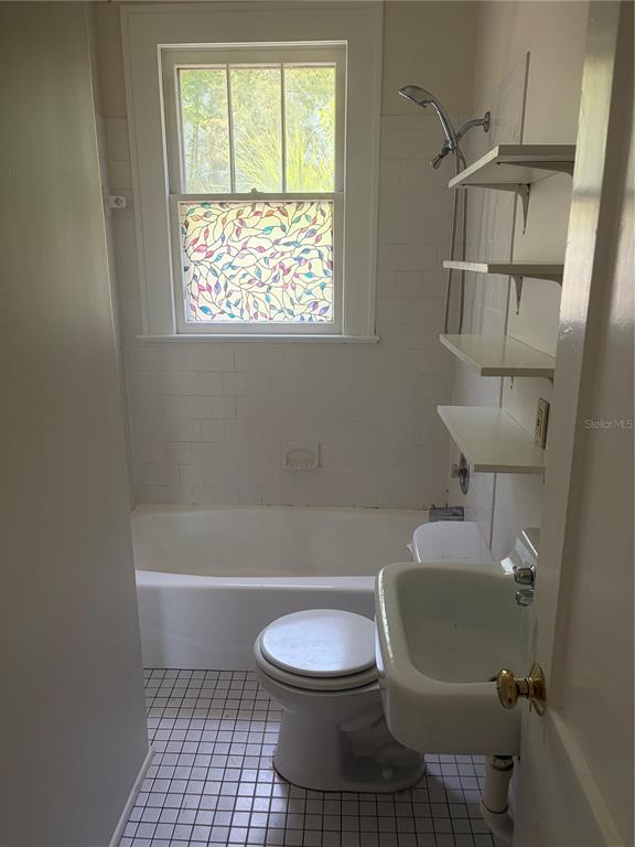 A small bathroom features a white bathtub, toilet, wall-mounted sink, and open shelving — 1555 7TH STREET, SARASOTA, FL