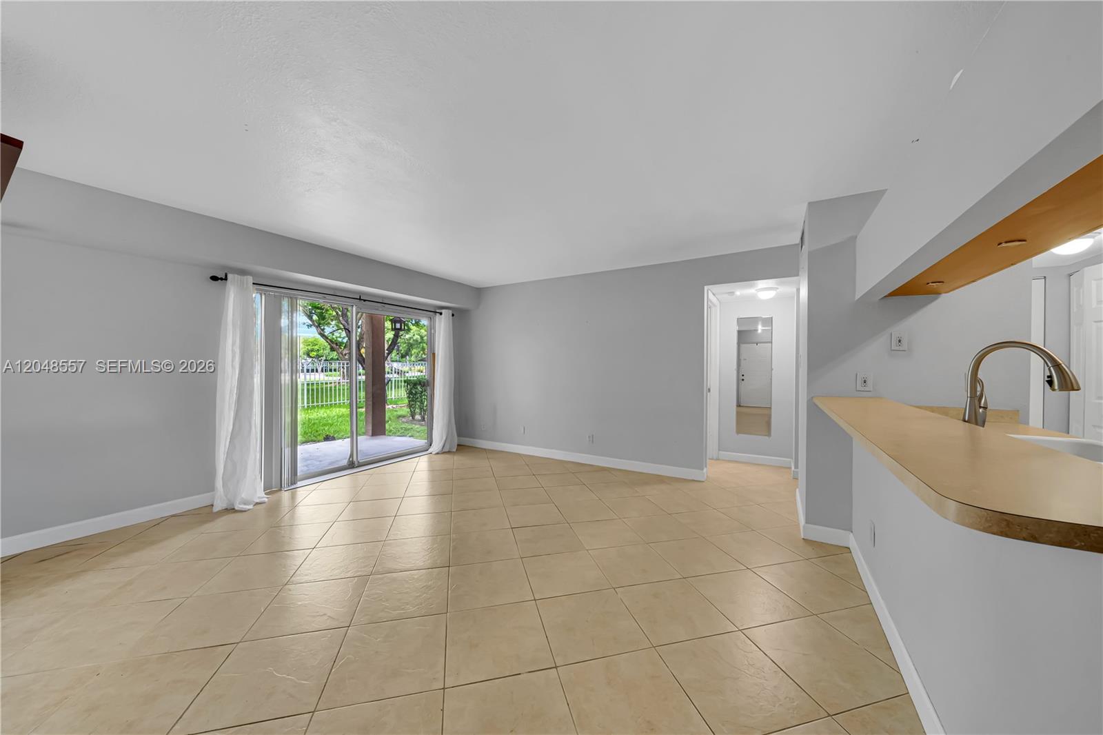 An empty room features light-colored tile flooring, gray walls, and a sliding glass door — 15770 SW 106th Ter # 106, Miami FL 33196, MIAMI, FL