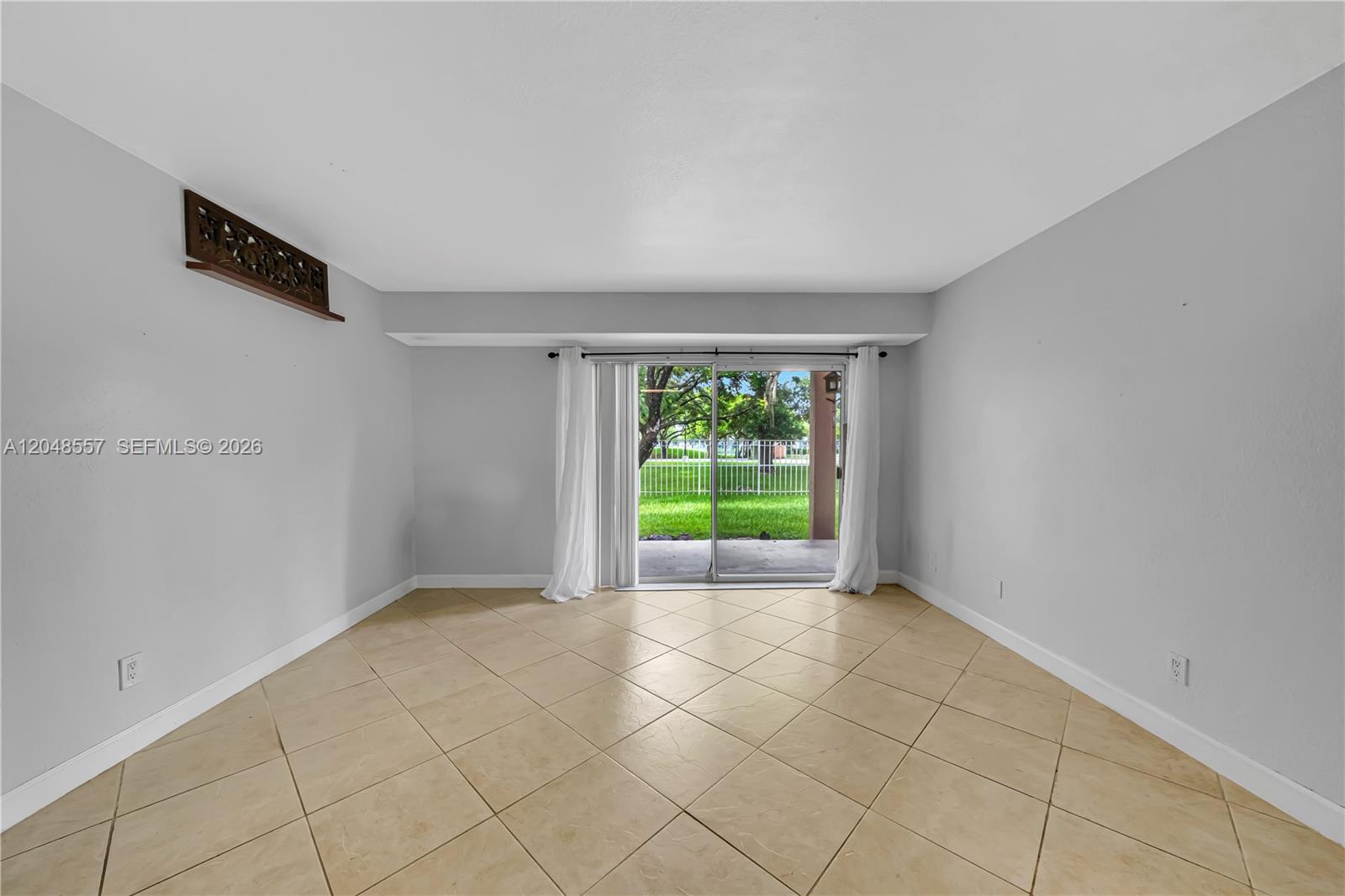 An empty living room features beige tile flooring, white walls, and a sliding glass door — 15770 SW 106th Ter # 106, Miami FL 33196, MIAMI, FL
