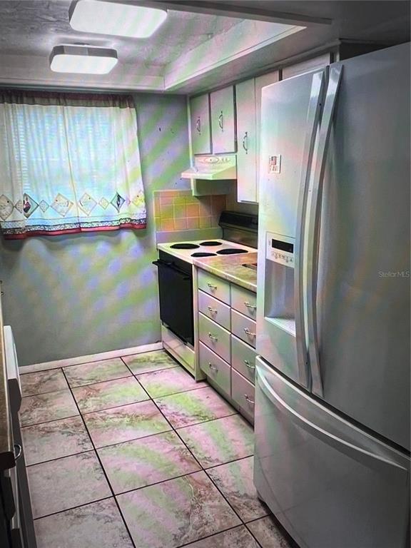 A kitchen features white appliances, light-colored cabinetry, a tiled floor, and a window with curtains — 7202 GULF HIGHLANDS DRIVE, PORT RICHEY, FL