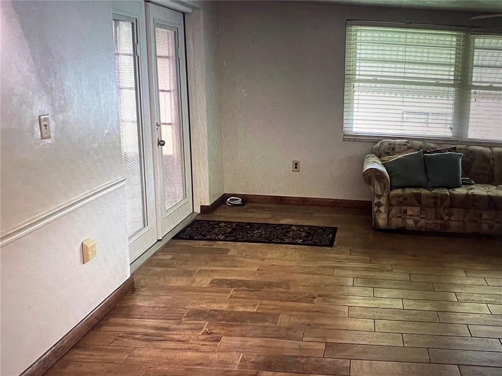 A room with wood-look tile flooring, a patterned sofa, and double glass doors — 7202 GULF HIGHLANDS DRIVE, PORT RICHEY, FL