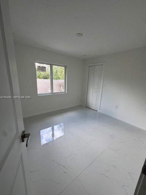 A bedroom with white walls, white marble-look tile flooring, a window, and a closet door — 3131 NW 60 St. # 0, Miami FL 33142, MIAMI, FL