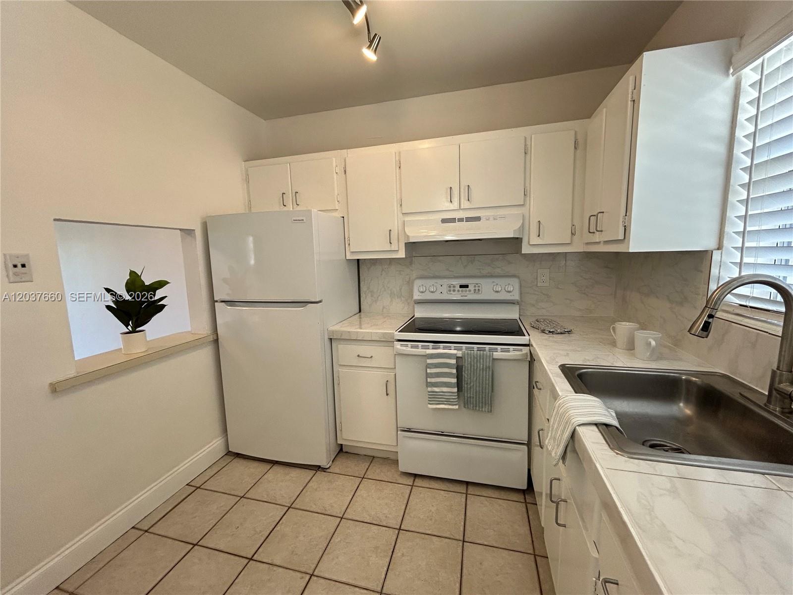 A small kitchen features white cabinets, white appliances, marble-look countertops, and beige tile flooring — 7505 SW 82nd St # 320, Miami FL 33143, MIAMI, FL
