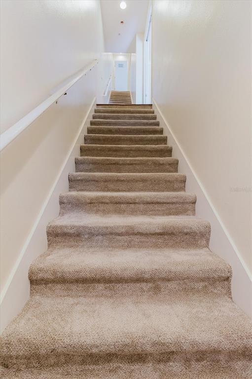 A straight staircase with beige carpet leads to an upper hallway with a white door — 6825 S KISSIMMEE STREET, TAMPA, FL