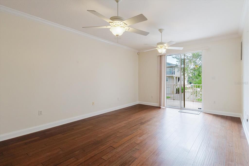 An empty room with hardwood floors, two ceiling fans, and a sliding glass door — 6825 S KISSIMMEE STREET, TAMPA, FL