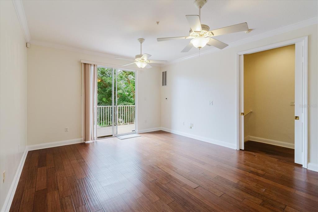 An empty room with hardwood floors, two ceiling fans, and a sliding glass door to a balcony — 6825 S KISSIMMEE STREET, TAMPA, FL