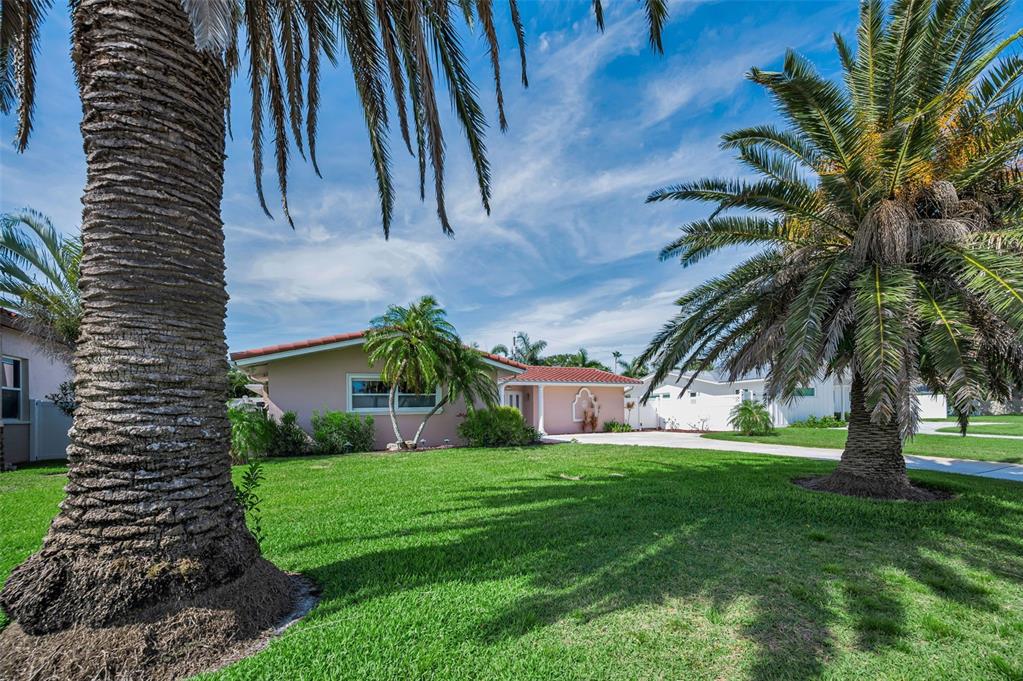 A single-story house with a pink exterior and a red tile roof sits behind palm trees — 111 17TH STREET, BELLEAIR BEACH, FL