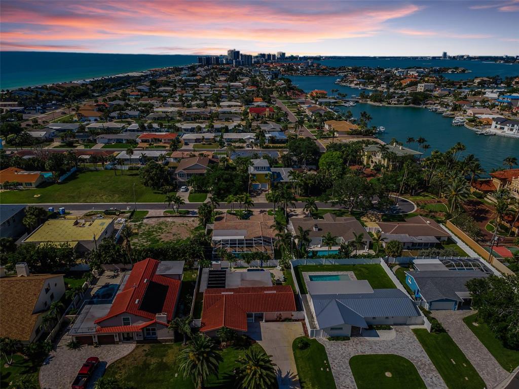 An aerial view shows residential homes, swimming pools, and a bay under a sunset sky — 111 17TH STREET, BELLEAIR BEACH, FL