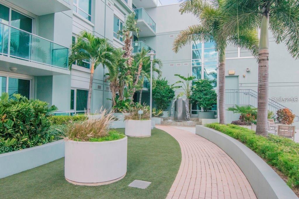 A paved walkway winds through a landscaped courtyard with a fountain and palm trees — 912 CHANNELSIDE DRIVE UNIT 2505, TAMPA, FL