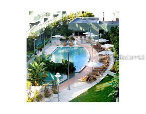 An elevated view of a swimming pool surrounded by lounge chairs, umbrellas, and lush landscaping — 912 CHANNELSIDE DRIVE UNIT 2505, TAMPA, FL