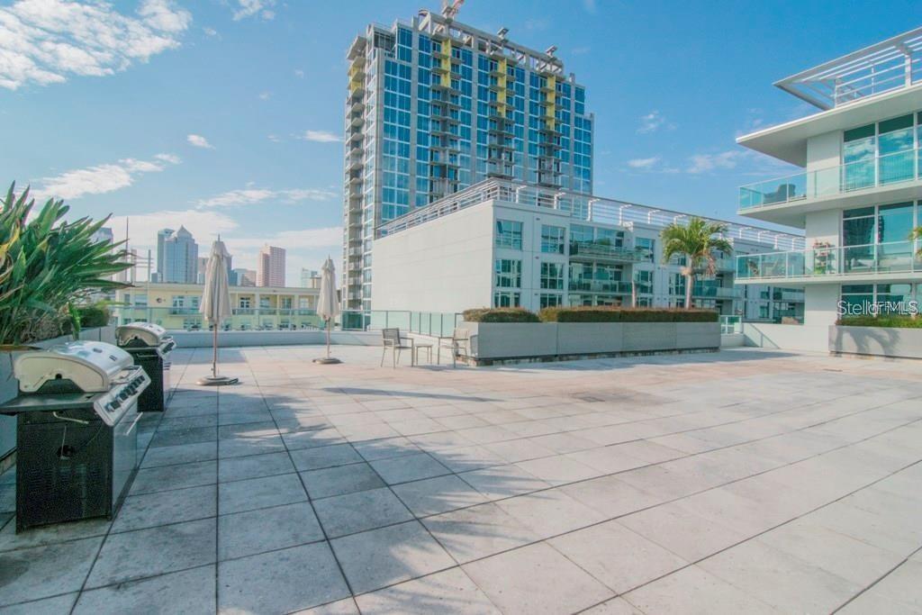 A rooftop terrace features tiled flooring, outdoor grills, patio umbrellas, and views of city buildings — 912 CHANNELSIDE DRIVE UNIT 2505, TAMPA, FL
