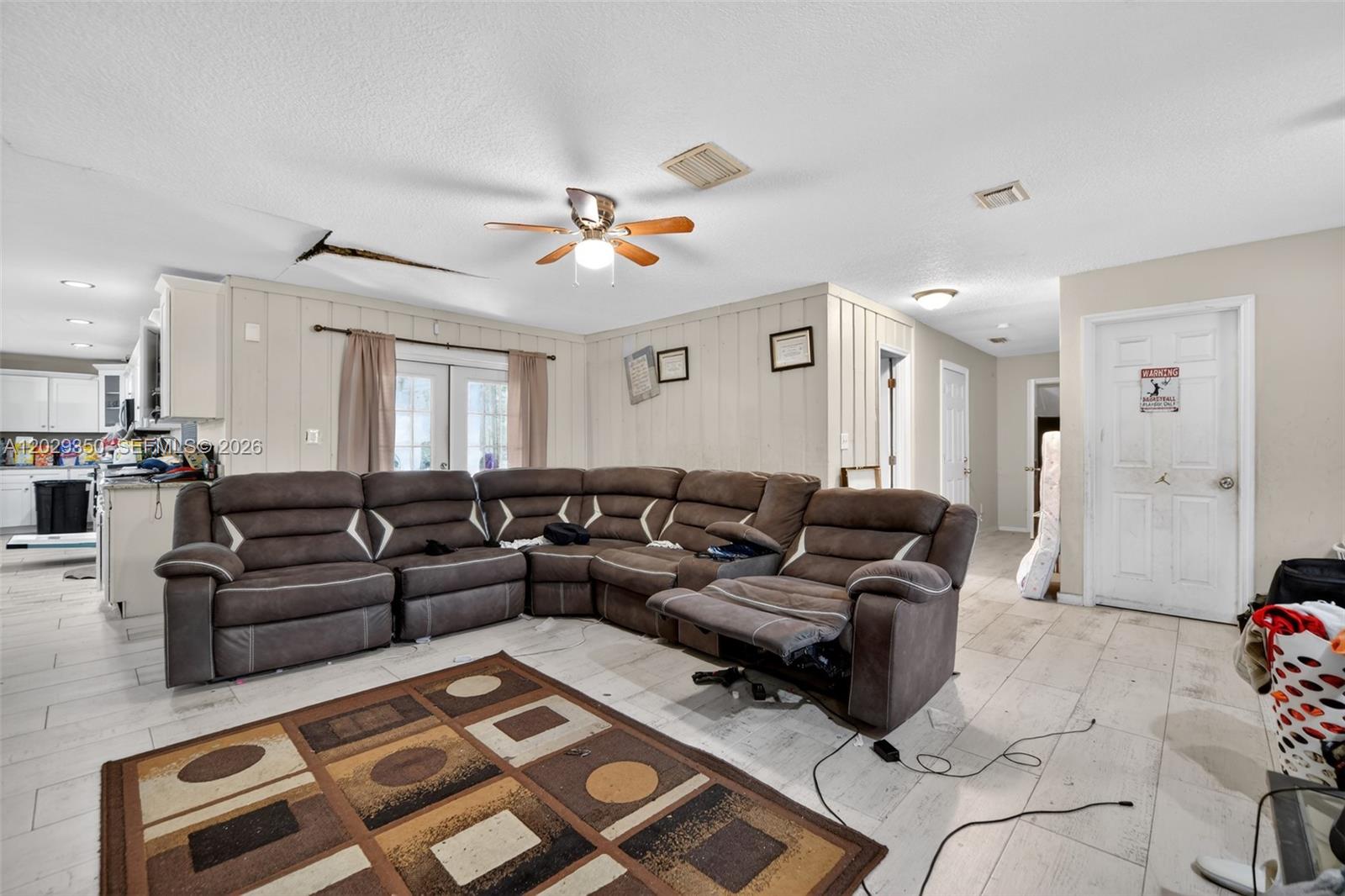 A living room features a large brown sectional sofa, tile flooring, and ceiling damage — 570 N HART BLVD, Orlando FL 32818, ORLANDO, FL