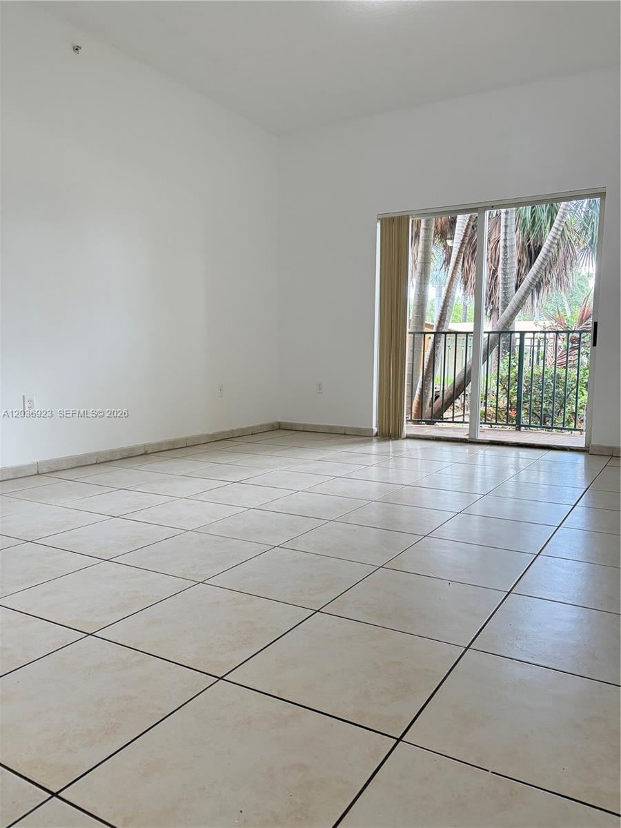 An empty room features light-colored tile flooring, white walls, and a sliding glass door — 7360 NW 114th Ave # 103, Doral FL 33178, DORAL, FL