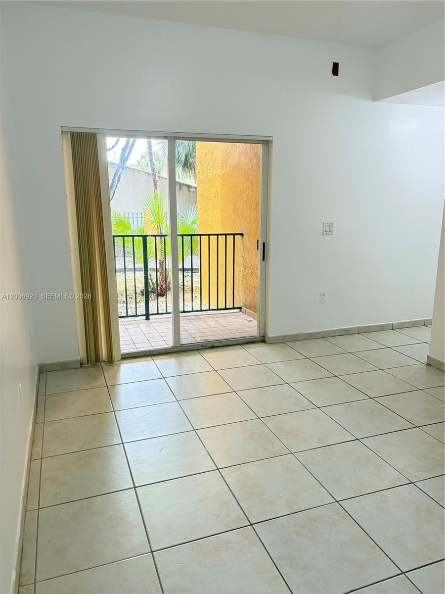 A room with light-colored tile flooring features a sliding glass door leading to a balcony — 7360 NW 114th Ave # 103, Doral FL 33178, DORAL, FL