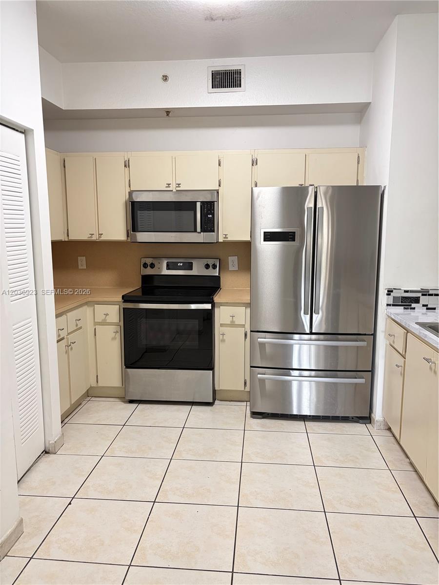 A kitchen features cream-colored cabinets, stainless steel appliances, and light-colored floor tiles — 7360 NW 114th Ave # 103, Doral FL 33178, DORAL, FL