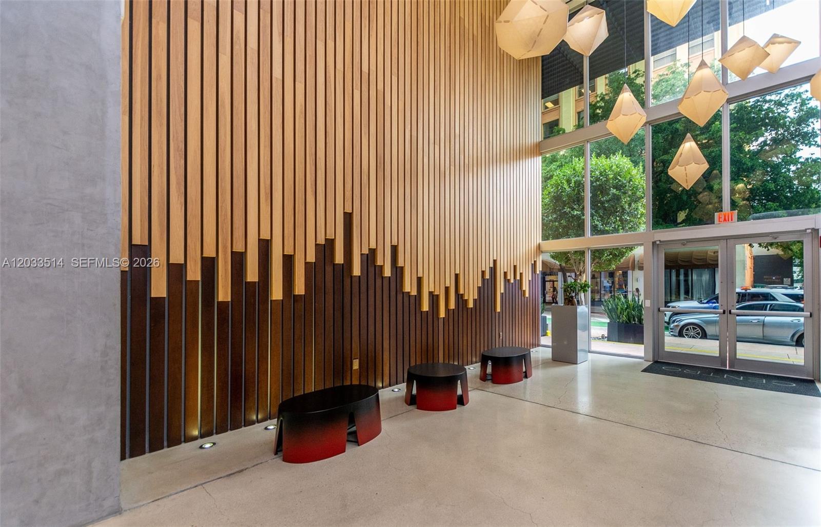 A modern lobby features a tall wood-slat accent wall, geometric pendant lights, and concrete flooring — 151 SE 1st St # 807, Miami FL 33131, MIAMI, FL