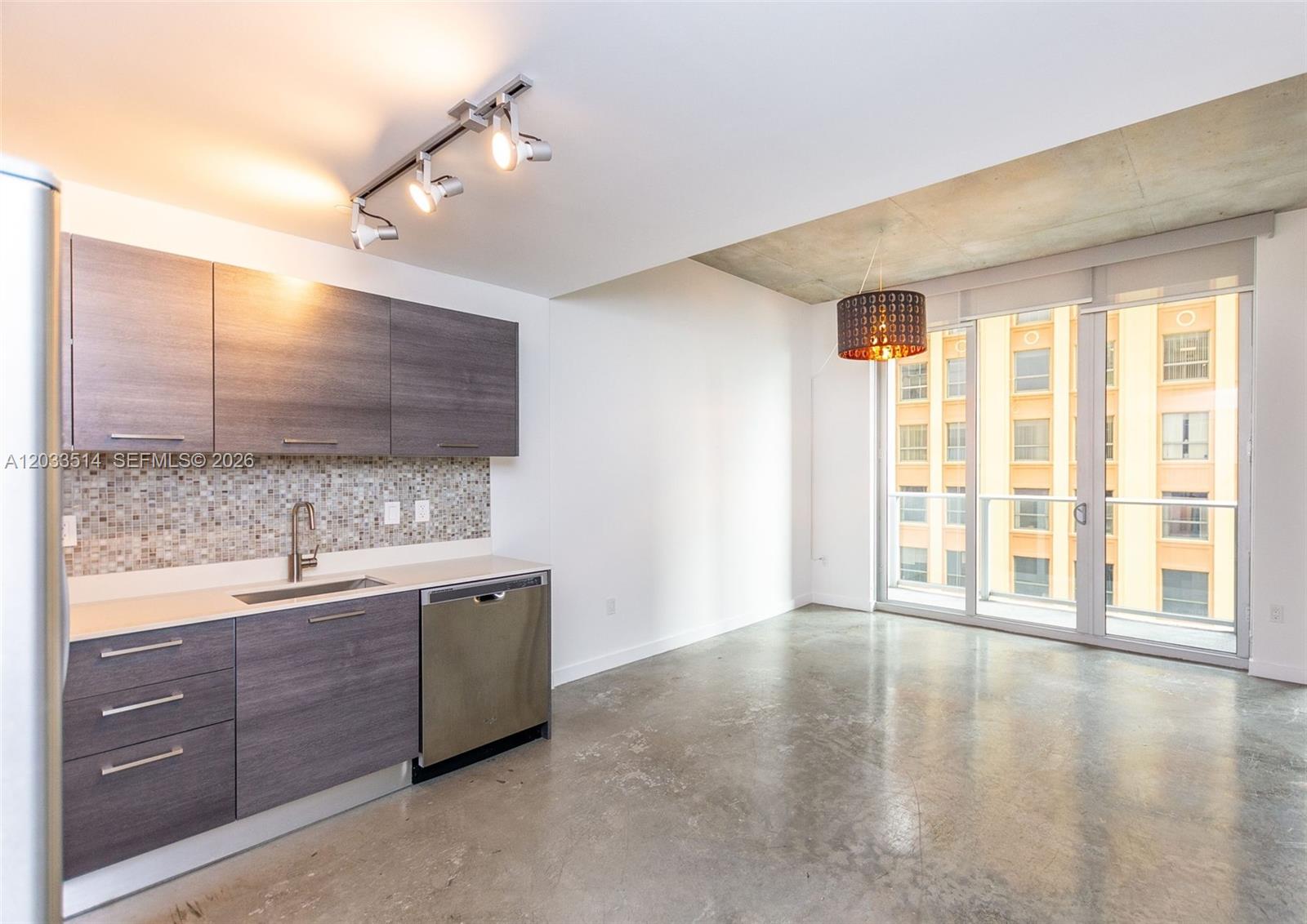 A modern kitchen with gray cabinets and concrete floors opens to a balcony with city views — 151 SE 1st St # 807, Miami FL 33131, MIAMI, FL