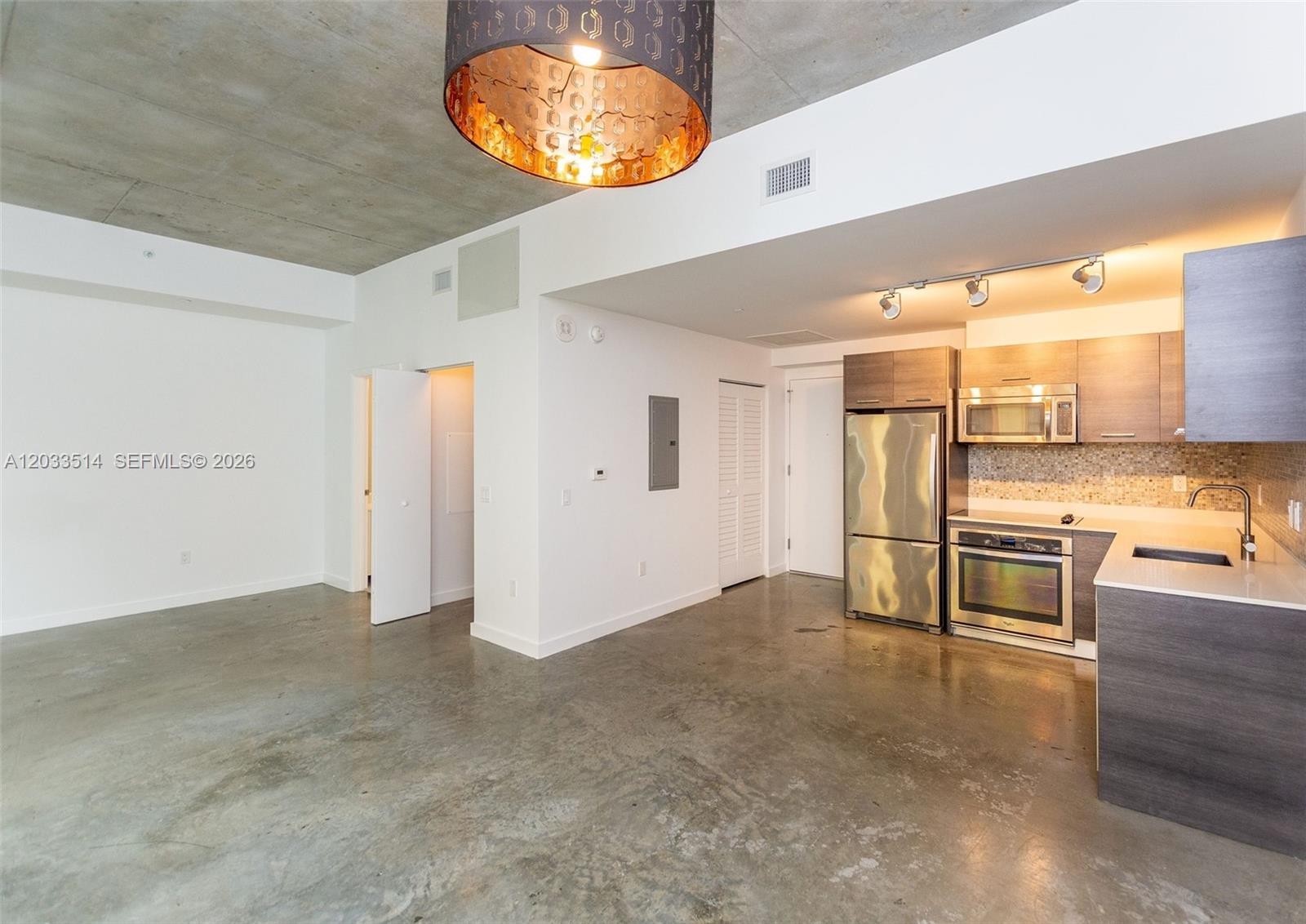 An open-concept kitchen and living area features concrete floors, a concrete ceiling, and stainless appliances — 151 SE 1st St # 807, Miami FL 33131, MIAMI, FL