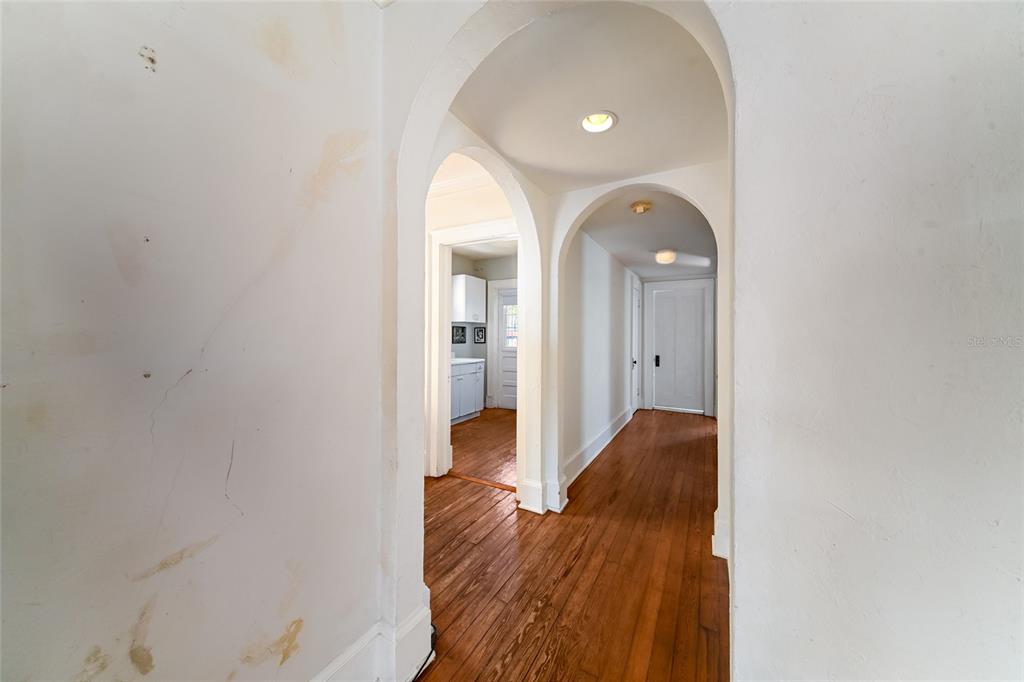 A hallway with arched doorways and hardwood floors leads to a kitchen and a door — 411 BURNS COURT, SARASOTA, FL