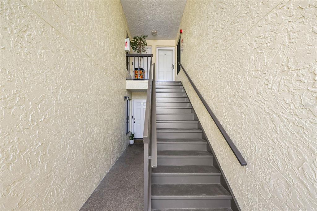 An outdoor staircase leads to two white apartment doors in a stucco-walled building — 7300 SUNSHINE SKYWAY LANE S UNIT 210, ST PETERSBURG, FL