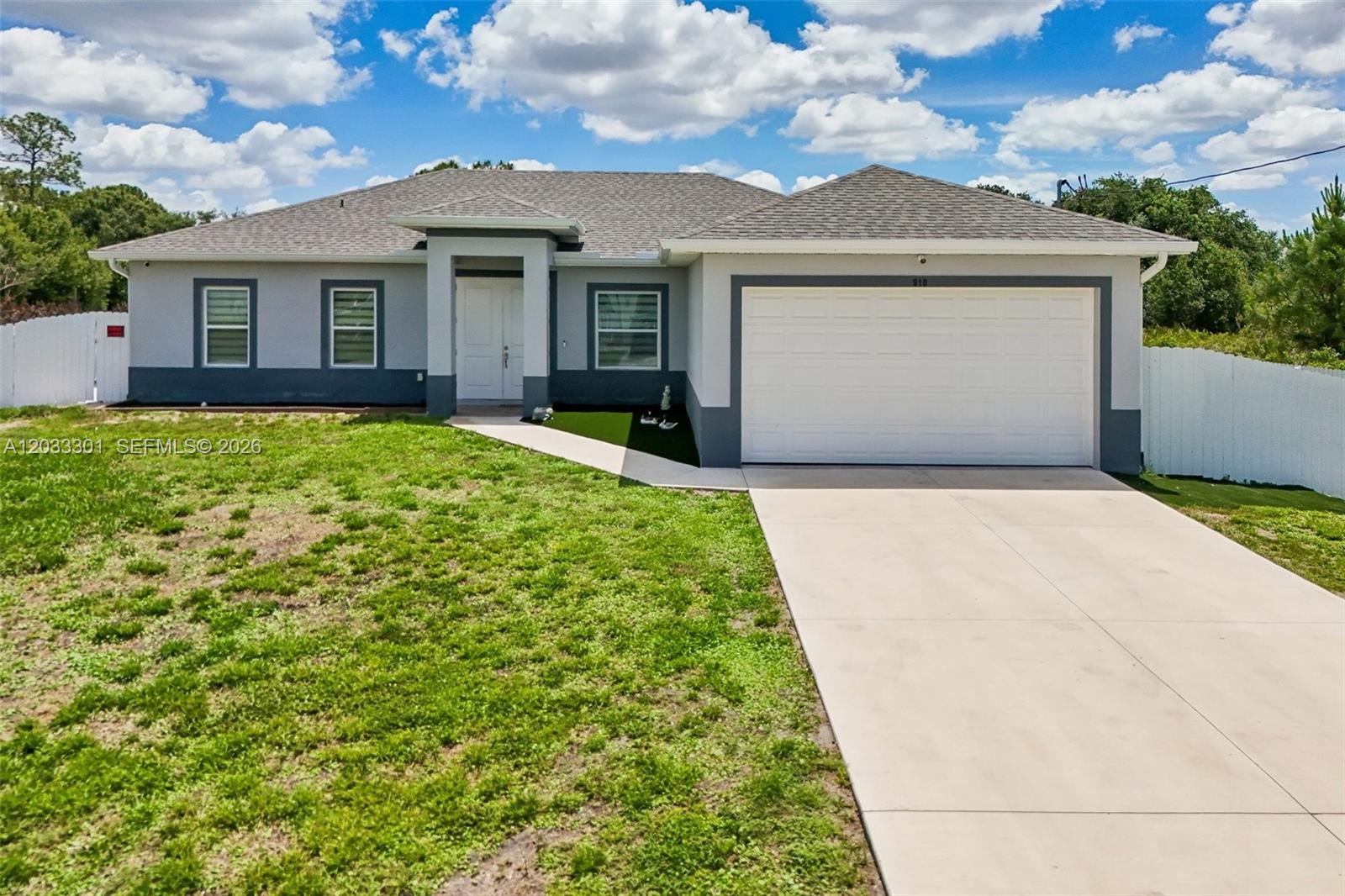 A single-story house with a gray exterior, white garage door, and a concrete driveway — 910 Richmond Ave N, Lehigh Acres FL 33972, LEHIGH ACRES, FL
