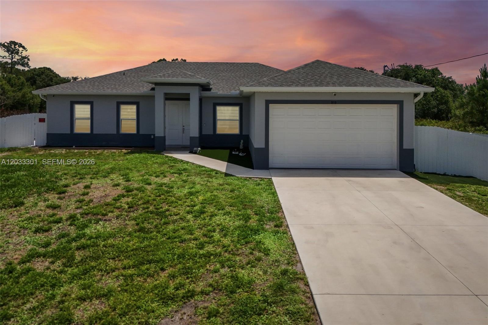 A single-story house with a gray exterior, a two-car garage, and a concrete driveway — 910 Richmond Ave N, Lehigh Acres FL 33972, LEHIGH ACRES, FL