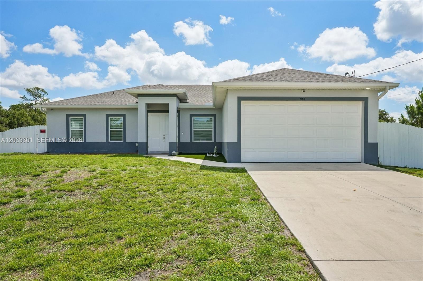 A single-story house with a white garage, gray exterior walls, and a front lawn — 910 Richmond Ave N, Lehigh Acres FL 33972, LEHIGH ACRES, FL