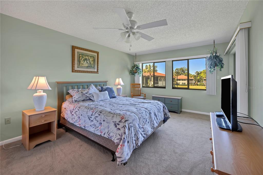 A bedroom features a bed, light green walls, a ceiling fan, and windows with exterior views — 5205 LAKE VILLAGE DRIVE UNIT 16, SARASOTA, FL