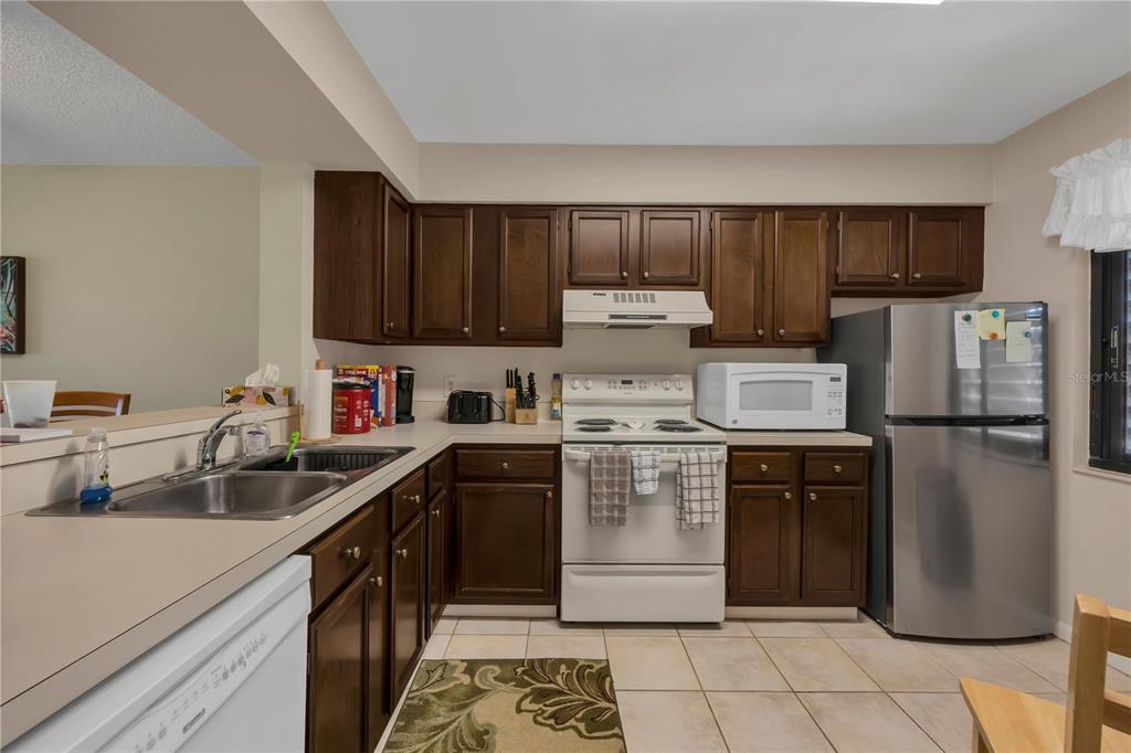 A kitchen features dark wood cabinets, white appliances, a stainless steel sink, and tile flooring — 5205 LAKE VILLAGE DRIVE UNIT 16, SARASOTA, FL