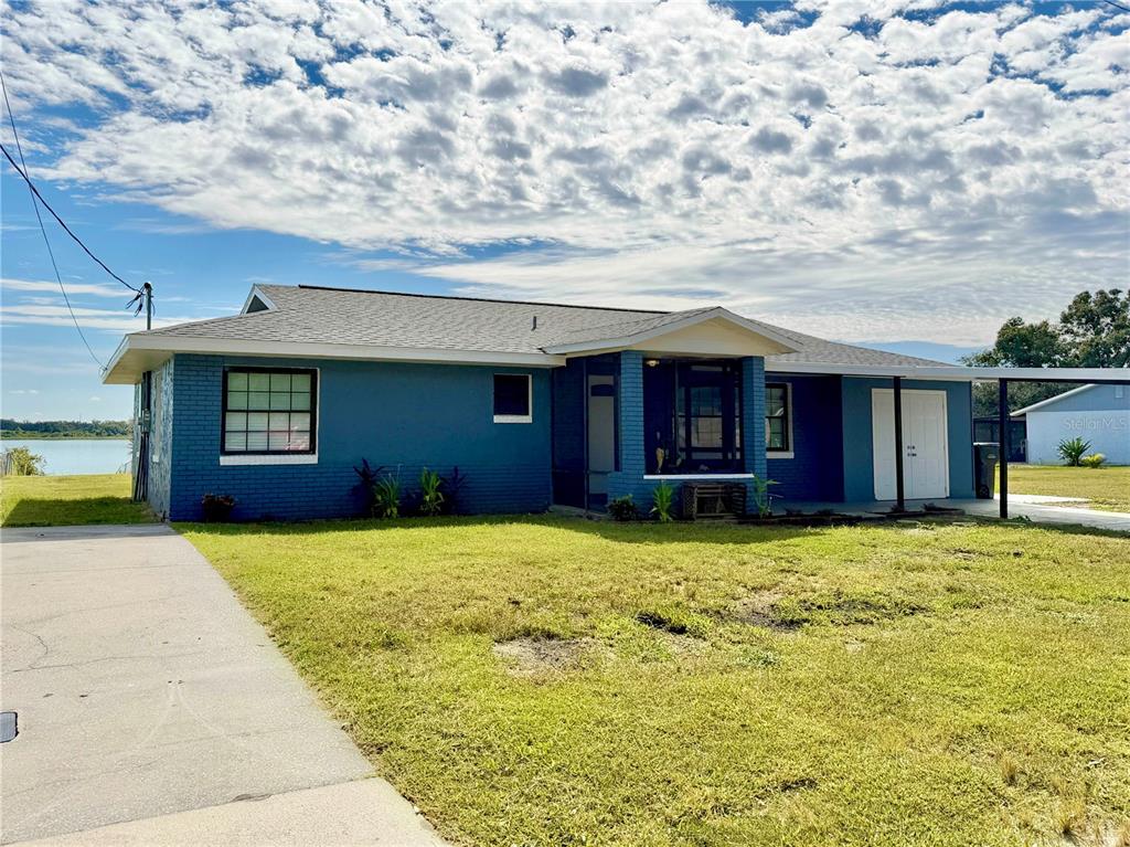 A blue brick house with a screened porch and a concrete driveway sits near water — 1151 CAREFREE COVE DRIVE, WINTER HAVEN, FL