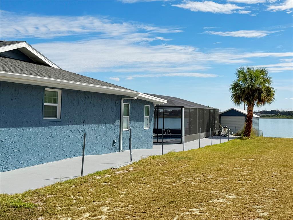 A blue house with a screened pool enclosure sits on a grassy waterfront lot — 1151 CAREFREE COVE DRIVE, WINTER HAVEN, FL