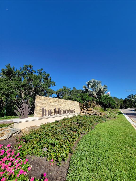 A stone monument sign for The Meadows stands beside a road with landscaping and trees — 3097 WILLOW GREEN UNIT 32, SARASOTA, FL