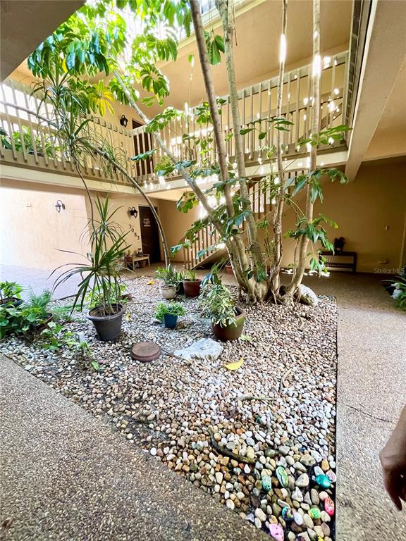An open-air courtyard features a gravel ground, potted plants, and a wooden staircase — 3097 WILLOW GREEN UNIT 32, SARASOTA, FL