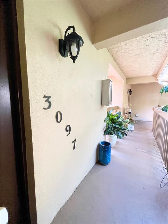 An exterior apartment hallway features a wall with the number 3091, a light fixture, and potted plants — 3097 WILLOW GREEN UNIT 32, SARASOTA, FL
