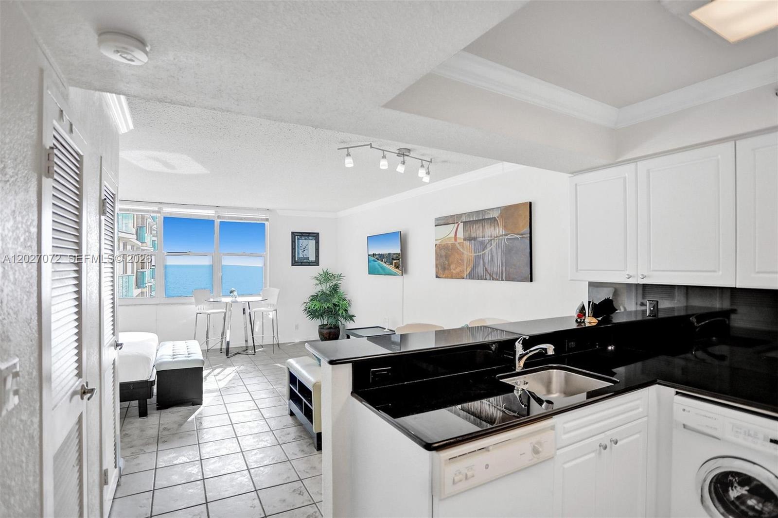 A kitchen with black countertops and white cabinets overlooks a living area with ocean views — 2501 S Ocean Dr, Hollywood FL 33019, HOLLYWOOD, FL